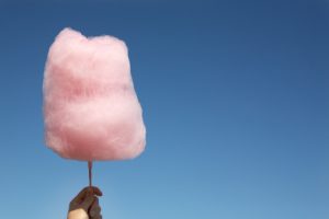 Pink cotton candy in hand on blue sky with copy space